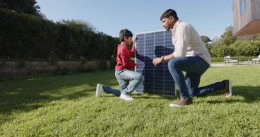 Hintli baba ve oğlu güneşli bir günde arka bahçeye güneş paneli kuruyorlar. Yenilenebilir enerji, aile, bağlanma, takım çalışması, sürdürülebilirlik