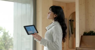 Gülümseyen kadın akıllı ev teknolojisini kontrol etmek için tablet kullanıyor. otomasyon, dijital, aygıt, kablosuz, yaşam tarzı, iç mekan