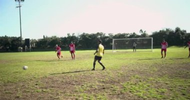Sahada futbol oynuyor, kaleci hazır, kaleye doğru koşan iki adam. Spor, rekabet, aksiyon, takım, açık hava, egzersiz