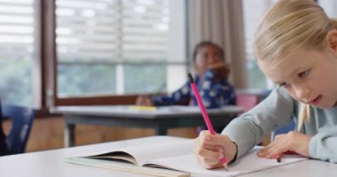 Okulda, masa başında not defterine yazan bir kız, işine konsantre oluyor. Eğitim, okula dönüş, öğrenme, öğrenme, çocukluk, konsantrasyon