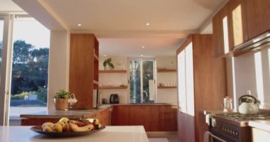 Ahşap dolapları ve tezgahında meyve kasesi olan modern mutfak, güneşli iç mekan, fotokopi alanı. Güneş ışığı, dekor