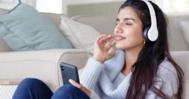 Evde dinlenen, kulaklıkla müzik dinlemekten hoşlanan akıllı telefon kullanan bir kadın. Rahatlama, teknoloji, rahatlık, rahatlık, dinleme, yaşam tarzı