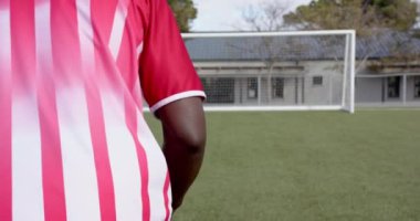 Futbol topu tutan, çizgili formalı Afro-Amerikan erkek sporcu sahada duruyor, fotokopi uzayı. Spor, rekabet, fitness, sahada, takım çalışması, eylem
