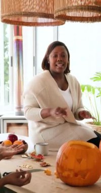 Dikey video: Afro-Amerikalı kadınlar birlikte balkabağı oyuyorlar, bayram sonbahar aktivitelerinin tadını çıkarıyorlar. Kutlama, aile, arkadaşlık, el işi, gelenek, mevsimlik