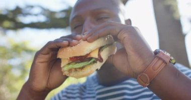 Hamburger yiyen, Afro-Amerikan bir adam arkadaşlarıyla parkta takılmaktan zevk alıyor. Yemek, arkadaşlık, eğlence, keyif, öğle yemeği, sosyal