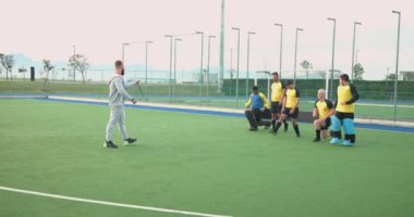 Erkek hokey takımı sahada antrenman yapıyor, oyuncular koçlarıyla çömelme hareketleri yapıyor. Spor, takım çalışması, fitness, egzersiz, koçluk, atletizm