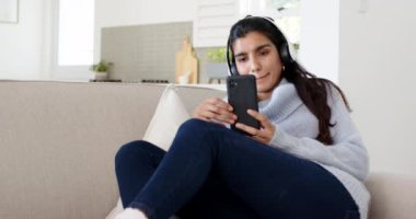 Evde dinlenen, akıllı telefondan kulaklıkla müzik dinleyen bir kadın. Boş zaman, rahatlama, teknoloji, yaşam tarzı, rahatlık, rahatlık.