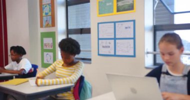 Okulda, dizüstü bilgisayar kullanan, kafasını kaşıyan, sınıftaki masada oturan bir kız. Eğitim, teknoloji, öğrenme, öğrenme, kafa karışıklığı, düşünme