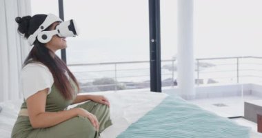 VR kulaklık kullanarak, Asyalı bir kadın spa ortamında yatakta dinleniyor, evde sanal deneyimin tadını çıkarıyor. Rahatlama, sağlık, teknoloji, güzellik, rahatlık, sanal gerçeklik.