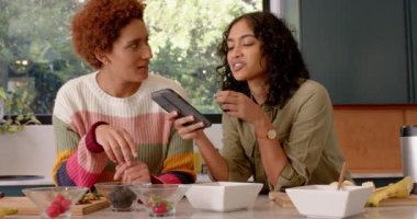 Bayan arkadaşlar mutfakta akıllı telefonlara bakarken gülüp sohbet ediyorlar. Sosyalleşme, teknoloji, kapalı alan, günlük yaşam tarzı, iletişim