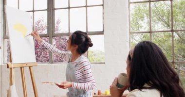 Arkadaşı evinde, parlak sanat stüdyosunda gözlemlerken, çok ırklı genç bir kadın tuvalde resim yapıyor. yaratıcılık, dostluk, hobi, ifade, konsantrasyon, ilham