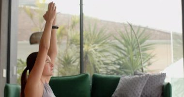 Evde meditasyon yapan, oturma odasında yoga yapan yeşil kanepeli bir kadın. Sağlık, farkındalık, rahatlama, egzersiz, egzersiz, sükunet.