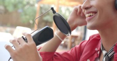 Gülümseyen genç çocuk evde mikrofon ve kulaklık kullanarak podcast yapıyor. Podcast, ses, ekipman, teknoloji, ev ofisi, kapalı alan