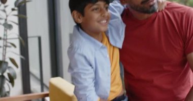 Gülümseyen genç çocuk Hintli babaya sarılıyor, içerde birlikte güzel vakit geçiriyorlar. Aile, bağ, mutluluk, ebeveynlik, aşk, çocukluk