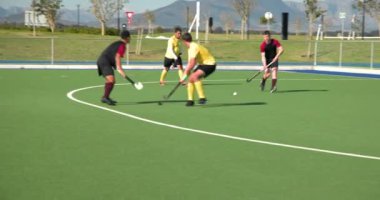 Çim hokeyi oynuyorlar, erkek oyuncular sahada kaleciyle etkileşime geçiyorlar. Spor, takım çalışması, yarışma, sporcular, açık hava, etkileşim