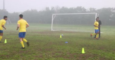 Futbolcular sahada külahlarla antrenman yapıyor ve sisli havada koçluk yapıyor. egzersiz, atlet, antrenman, açık hava, futbol