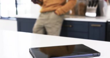 Evde, rahat kazaklı bir adam modern mutfakta akıllı telefon kullanıyor. Teknoloji, yaşam tarzı, iletişim, rahatlama, gündelik, yerli