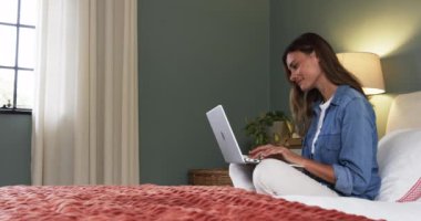 Evde dinlenen, dizüstü bilgisayar kullanan, memnun ve düşünceli görünen bir kadın, kopyalama alanı. Yaşam tarzı, rahatlama, teknoloji, konfor, yatak odası, gezinme