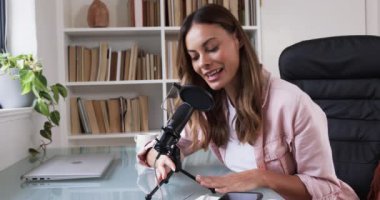 Kadın merkez ofiste mikrofon ve dizüstü bilgisayarla podcast kaydediyor. Podcast, yayıncılık, teknoloji, ekipman, yaratıcı, ses