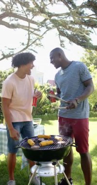 Dikey video: Arkadaşlar dışarıda barbekü yapmayı, içkilerle kadeh kaldırmayı ve ızgara yemeği seviyorlar. Kutlama, parti, toplanma, yaz