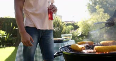 Mısır ve et ızgara, iki çok ırklı erkek arkadaş açık hava barbeküsünde içkiyle kadeh kaldırıyor. Kutlama, arkadaşlar, yaz, açık hava, yemek, toplanma