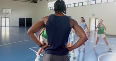 Koç, bayan basketbolcuları spor salonunda top sürme ve defans antrenmanı yaparken izliyor. Spor, koçluk, antrenman, takım çalışması, fitness, egzersiz