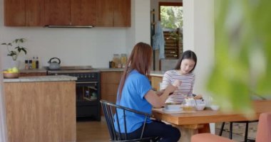 Birlikte kahvaltı ediyoruz, Asyalı anne ve kızı mutfak masasında yemeğin tadını çıkarıyorlar. Aile, kaynaşma, birliktelik, ebeveynlik, sabah, yemek zamanı.