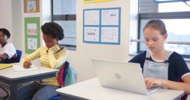 Okulda, dizüstü bilgisayar kullanan ve başka yere bakan bir kız, sınıfta masa başında oturuyor. Eğitim, teknoloji, öğrenme, öğrenci, öğrenim, çocukluk