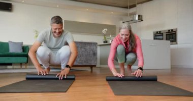 Yoga minderlerini sarmak, çok ırklı bir çiftin evde eğlenmesi. fitness, wellness, happiness, lifestyle, exercise, relaxation