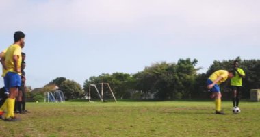 Sahada futbol oynamak, takım arkadaşları izlerken yeşil formalı bir sporcunun topa vurması. Spor, takım çalışması, rekabet, eylem