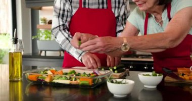 Mutfakta kıdemli bir çift şenlik yemeği hazırlıyor, evde sebzelere yağ döküyor. Yemek pişirme, yaşlılık, yaşam tarzı, tatil, yemek hazırlama, sağlıklı beslenme
