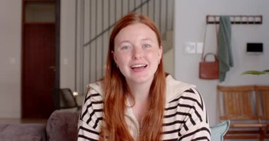 Kanepede oturan, video görüşmesinde konuşan kızıl saçlı, gülümseyen kadın. Arkadaşlık, rahatlama, mutluluk, rahatlık, sosyalleşme, neşe