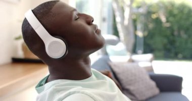 Kulaklıkla müzik dinleyen Afro-Amerikan bir adam evdeki kanepede dinleniyor. Rahatlama, rahatlama, rahatlama, rahatlama, ses