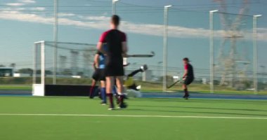 Çim hokeyi oynayan erkek sporcular yeşil sahada yoğun bir maçta yarışıyorlar. Spor, takım çalışması, rekabet, yoğunluk, açık hava, egzersiz