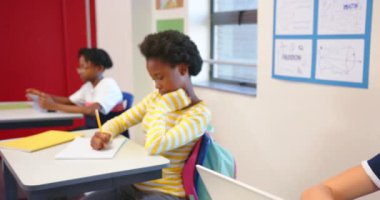 Okulda, çocuklar sıralarda çalışıyor, biri deftere yazıyor, biri tablet kullanıyor. Eğitim, öğrenme, teknoloji, sınıf, öğrenciler, çocukluk