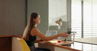 Akıllı telefondan konuşmak, ev ofisinin masasında dizüstü bilgisayarla çalışan bir kadın. Uzaktan çalışma, telekomünikasyon, iş, teknoloji, çoklu görev, iletişim
