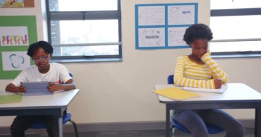 Okulda, masada elinde defterle oturan bir kız, sınıfta düşünceli görünüyor. Eğitim, öğrenim, öğrenim, çocukluk, öğrenci