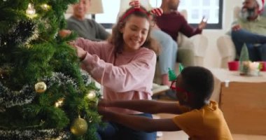 Kardeşler ve aile Noel ağacını birlikte süslüyor, evdeki mutlu anları paylaşıyorlar. bayram, kutlama, şenlik, birliktelik, gelenek, süsler