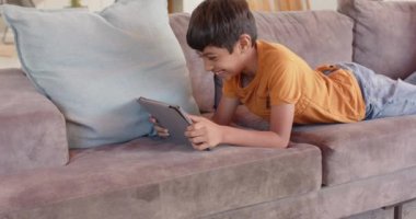 Kanepede uzanmak, tablet kullanan ve gülümseyen bir çocuk, evde boş vakitlerin tadını çıkarmak. Teknoloji, rahatlama, mutluluk, çocuk, dijital, yaşam tarzı