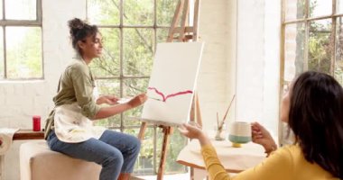 Arkadaşı parlak ev stüdyosunda kahvenin tadını çıkarırken, kadın ressam tuvalde resim yapıyor. yaratıcılık, dostluk, rahatlama, arkadaşlık, ilham, canlı