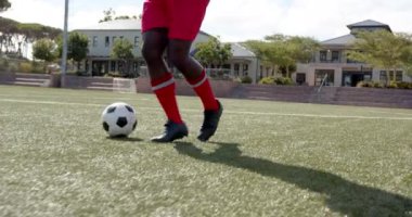 Sahada futbol oynayan, kırmızı üniformalı Afro-Amerikan erkek sporcu top sürüyor, fotokopi çekiyor. Spor, takım çalışması, rekabet, atletik, aksiyon, fitness
