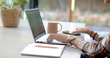 Akıllı telefon ve dizüstü bilgisayar kullanan, evde masa başında çalışan genç bir çocuk. Uzaktan çalışma, ev ofisi, teknoloji, üretkenlik, iş yeri, çalışma alanı