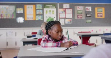 Okulda, masa başında not defterine yazı yazan bir kız, sınıf çalışmalarına odaklanıyor. Eğitim, okula dönüş, öğrenme, öğrenme, çocukluk, öğrenci