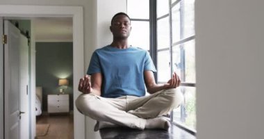 Pencere kenarında meditasyon yapan, mavi gömlekli rahat bir adam evinde huzur buluyor. Farkındalık, rahatlama, sükunet, dinginlik, zen, sakinlik