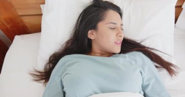 Yatakta uzanmış, Asyalı bir kadın tapınaklara masaj yapıyor ve gözleri kapalı evde dinleniyor. Rahatlama, masaj, kendine bakım, sağlık, stres atma, sükunet.