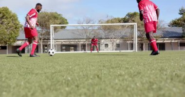 Futbol oynuyorlar, kırmızı üniformalı Afro-Amerikan adamlar sahada kalecilik yapıyorlar, kopyalama sahası. Spor, takım çalışması, antrenman, sporcular, yarışma, egzersiz