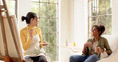 Arkadaşı evde kahve içip sohbet ederken, kadın ressam tuvalde resim yapıyor. yaratıcılık, hobi, arkadaşlık, yaşam tarzı, rahatlama, yerli