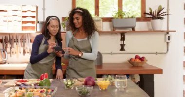 Mutfakta, evde sebze hazırlarken akıllı telefonu paylaşan iki çok ırklı bayan arkadaş. Arkadaşlık, yemek pişirme, kahkaha, eğlence, bağlanma