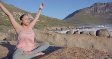 Okyanusun yakınındaki kayalarda bağdaş kurmuş, Asyalı bir kadın dışarıda meditasyon yapıyor. Meditasyon, farkındalık, sükunet, doğa, huzur, rahatlama.