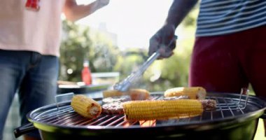 Mangalda mısır ve et ızgara, dışarıda takılmaktan hoşlanan iki çok ırklı erkek arkadaş. Yaz, arkadaşlar, yemek, eğlence, yemek, keyif